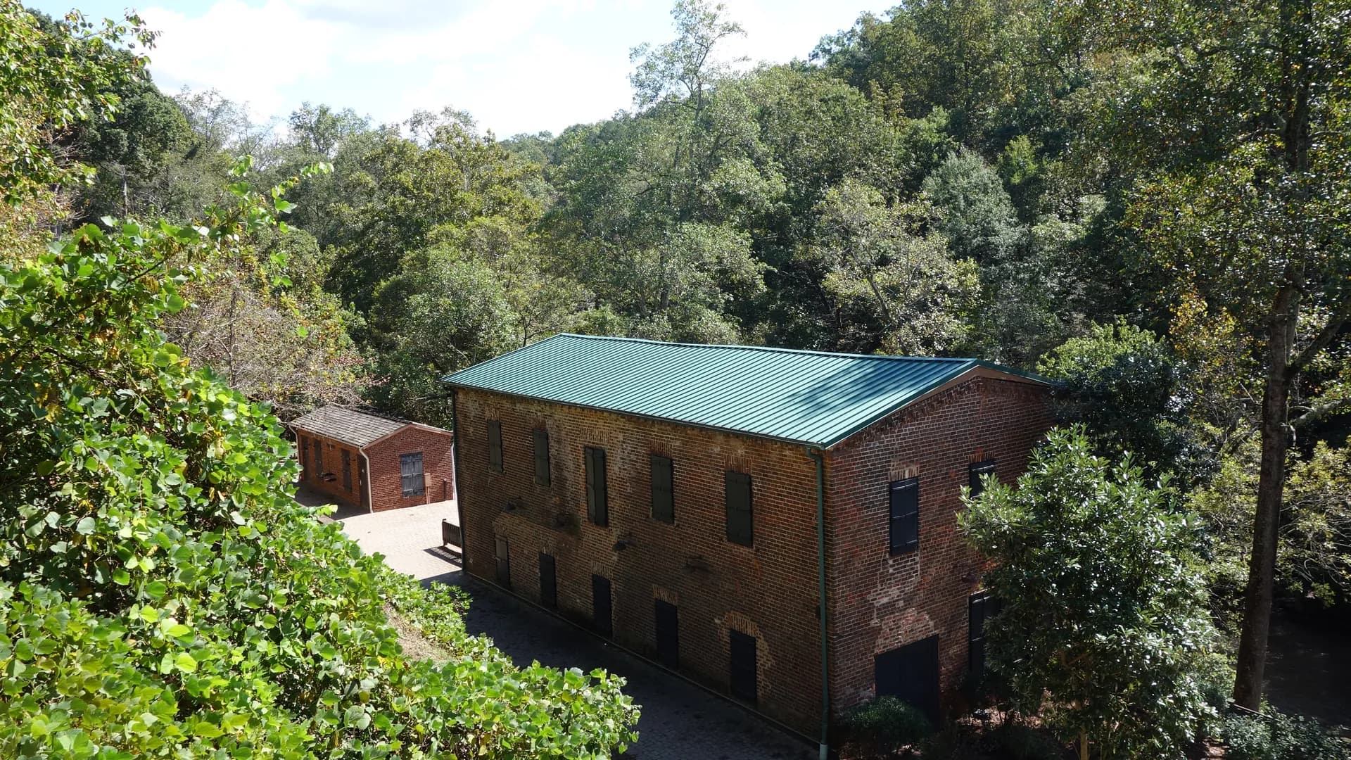 The historic brick Old Mill Machine Shop with a green roof among trees in Roswell, Georgia.